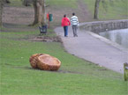 An image of the benches from a distance with two blokes walking around the lake, and the original park furniture in the backgrou