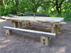 A massive banquet table positioned in the shade, with a bottle of beer on the top of it, which looks miniscule and out of propor