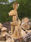 A roughed out rabbits sits aloft of a large woodpile