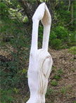 A tall thin lady stands with her hands upright, hair covering her breasts, protruding from a log