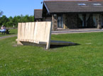 An empty sun kissed bench, with the Bryn Bach Park visitor centre in the frame