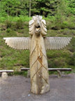 Front view of a massive totem pole which has a head a bit like an eagle, and wings