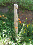Two tall thin wooden statues closely coupled, photographed from the side