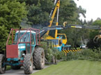 A large tractor and crane work together to clean up the site of a large tree fell